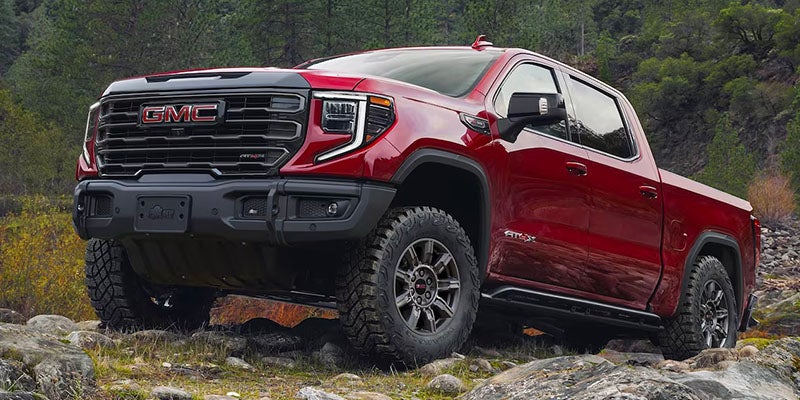 2025 GMC Sierra Denali in red driving off-road on a grassy hill
