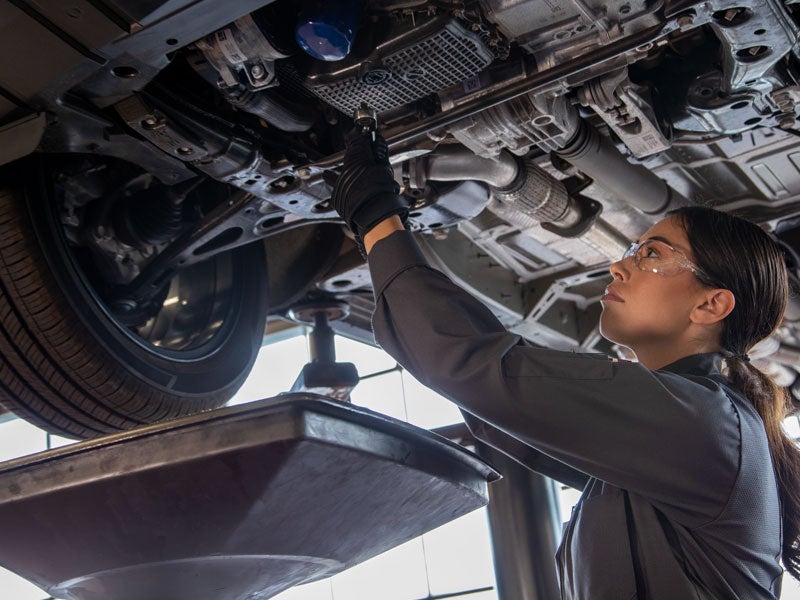 A technician removing the drain plug from under a vehicle.